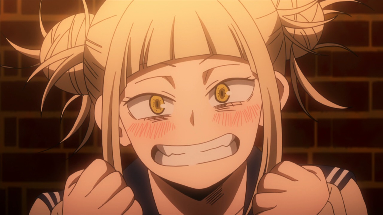 personagem Himiko Toga do anime Boku no Hero, ela tem cabelos loiros lisos e amarrados em dois coque laterais e franja, olhos castanhos claros, está sorrindo e corada e veste uma roupa colegial estilo japonês, ao fundo as paredes de tijolos