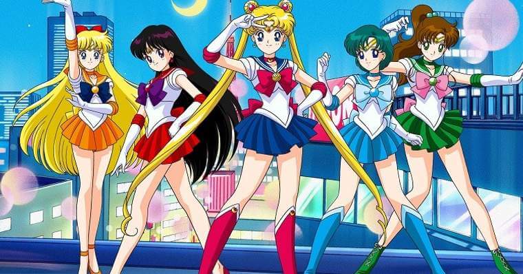 5 personagens do anime sailor moon, todas vestem vestidinho curto colegial, cada uma com uma cor, esquerda para direita temos a primeira com cabelos longos loiros com vestido laranja e laço azul escuro, segunda com cabelos pretos longos e vestido vermelho com laço roxo, no meio uma de cabelos loiros longos amarrados em dois coques laterais, vestido azul e laço vermelho, a quarta tem cabelos curtos verdes e vestido e laço azul claro, a quinta tem cabelos castanhos amarrados e usa vestido verde com laço rosa, ao fundo a cidade de toquio a noite e uma lua crescente