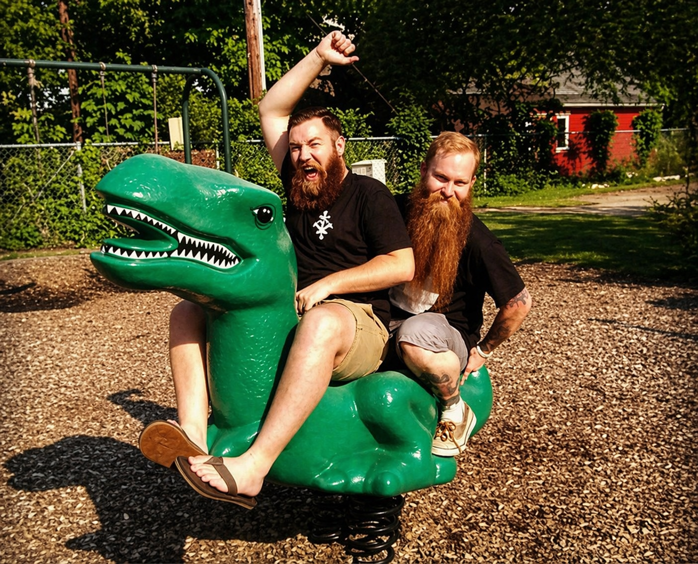 Cartoon: two adult bearded men riding a plastic Tyrannosaurus rex figure