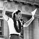 An image of a man with his hands up in the air in a celebratory pose looking out of the frame. It seems as if he's speaking to a crowd of people.