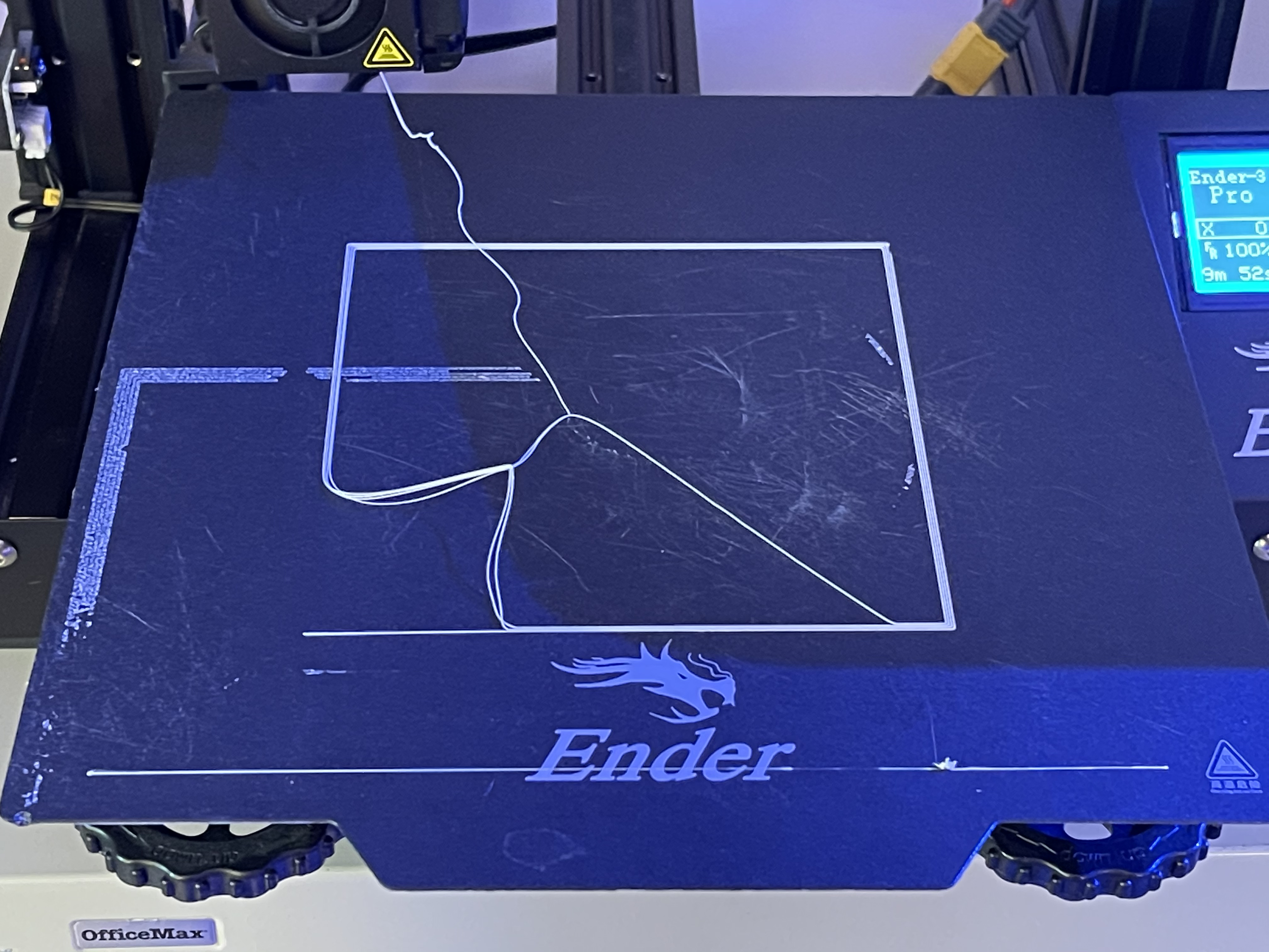 An image of a 3D printing bed with plastic that has peeled off of the bed and stuck to the nozzle.