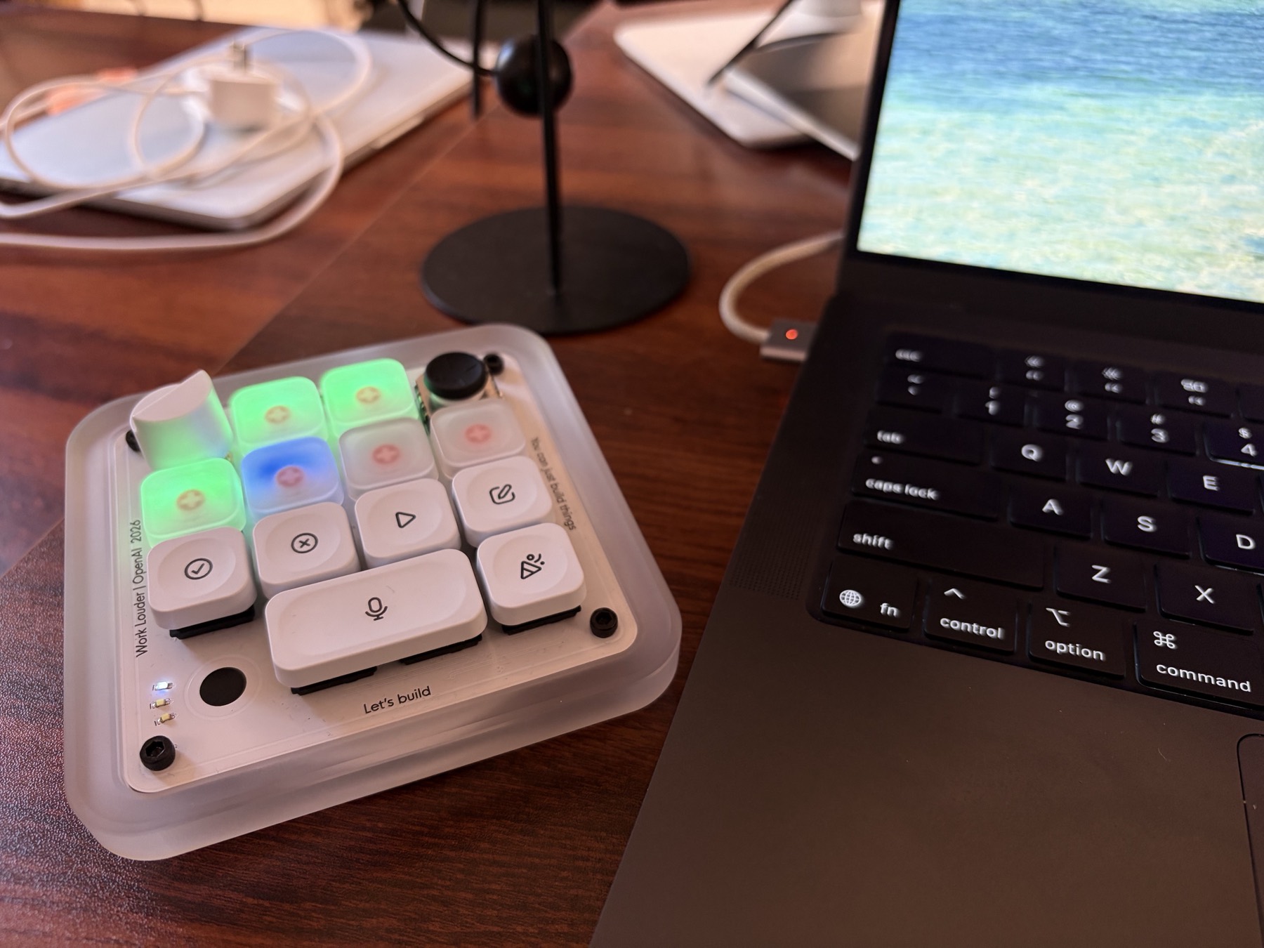 A Codex Micro beside a MacBook, its keys lit green, blue and amber for different sessions