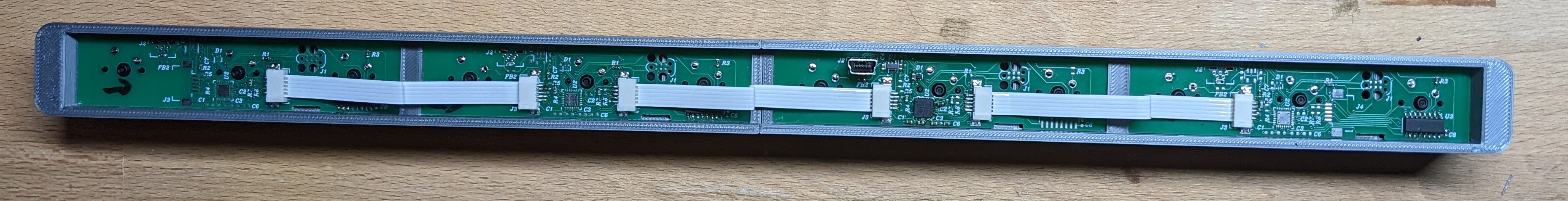 Photo of four green circuit boards in a 3D printed shell connected with white FFC cables.
