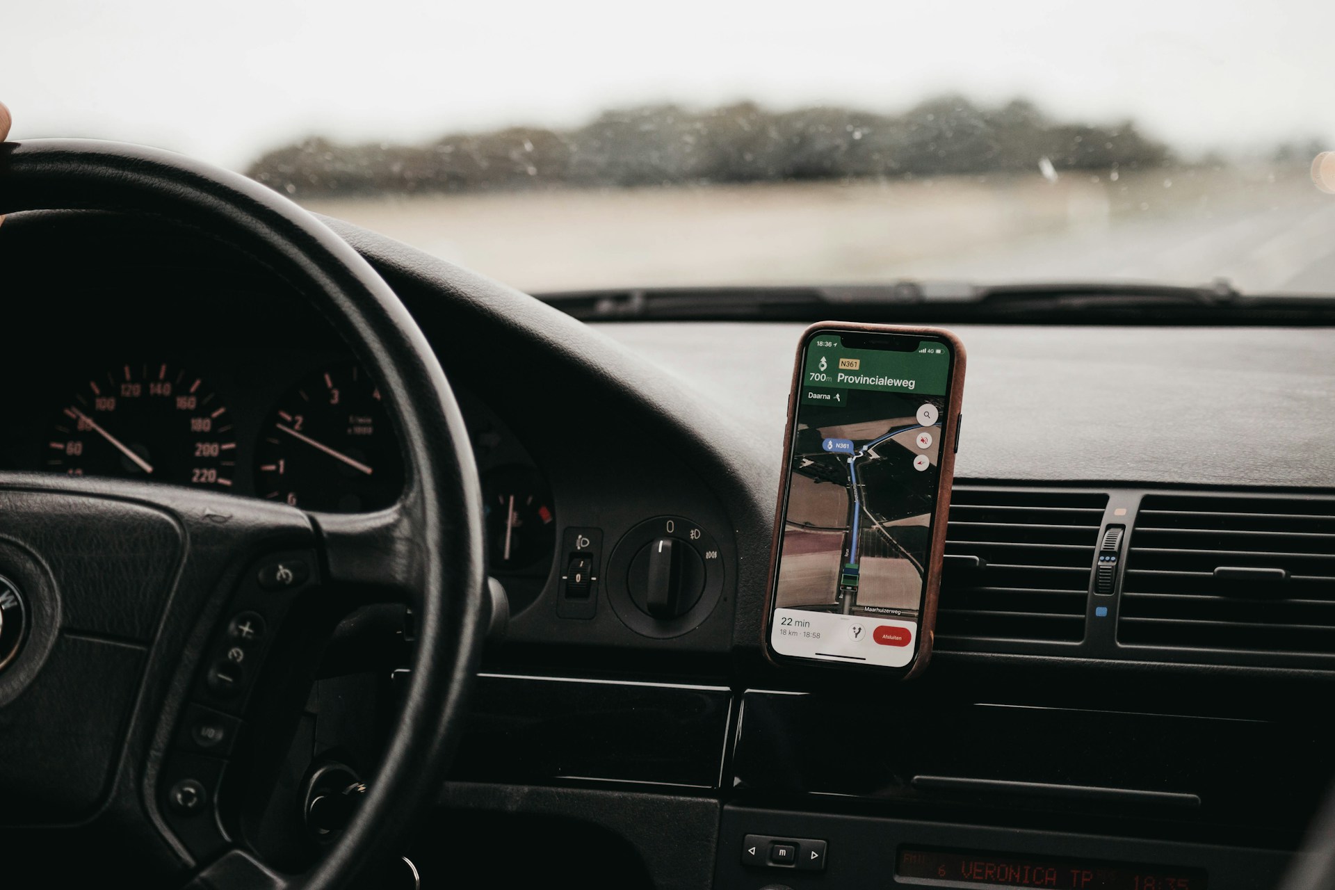 A driver's phone mounted on the dashboard showing a navigation app while driving
