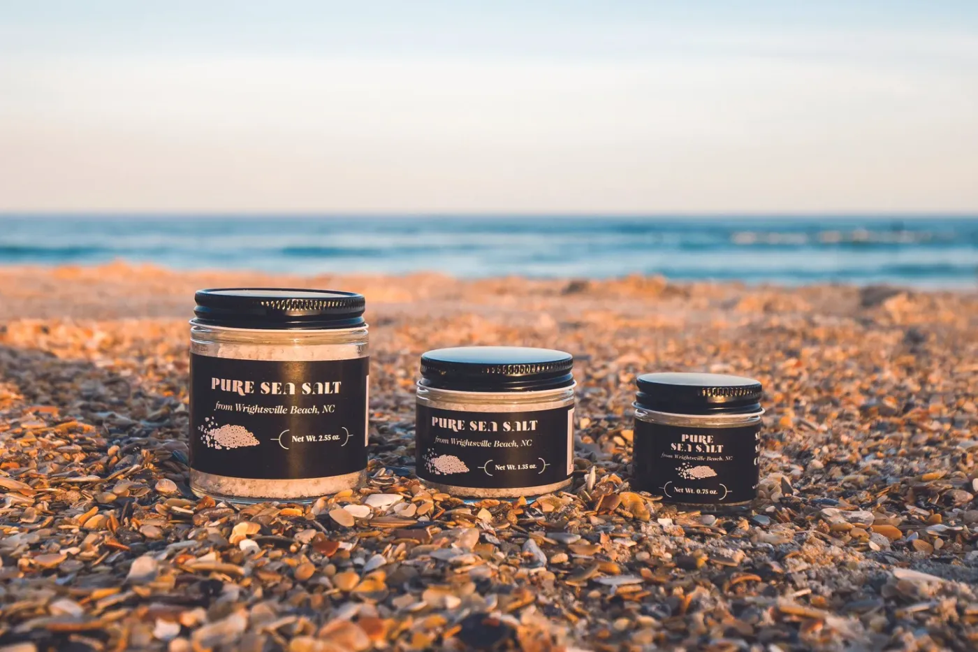 Jars of Sea Love Pure Sea Salt from Wrightsville Beach NC on the sand with the Atlantic Ocean behind them