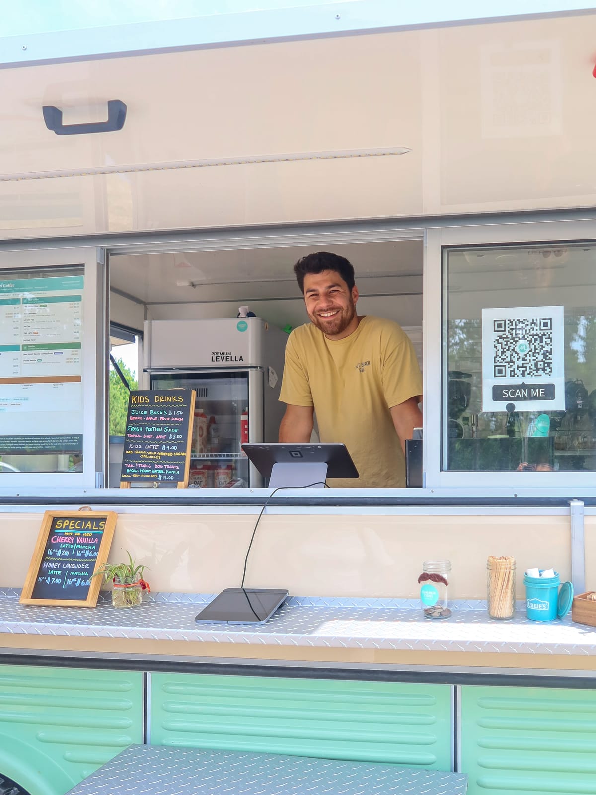 Zack Bennett, founder and barista of Common Tides Coffee, smiling from the service window of his mobile coffee trailer in Wilmington NC