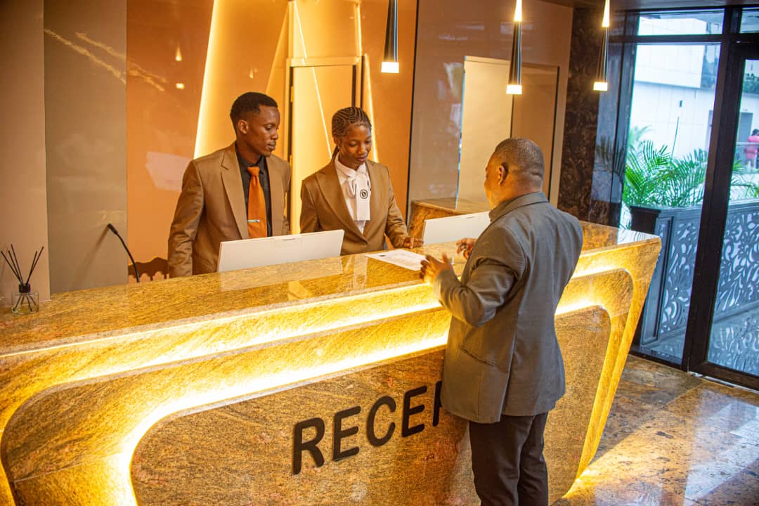 The Royal Reception desk at Frank N Hotels Royal — warm gold light, uniformed staff, and a guest being welcomed