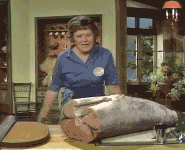 Julia Child brandishing cutlery over a fish