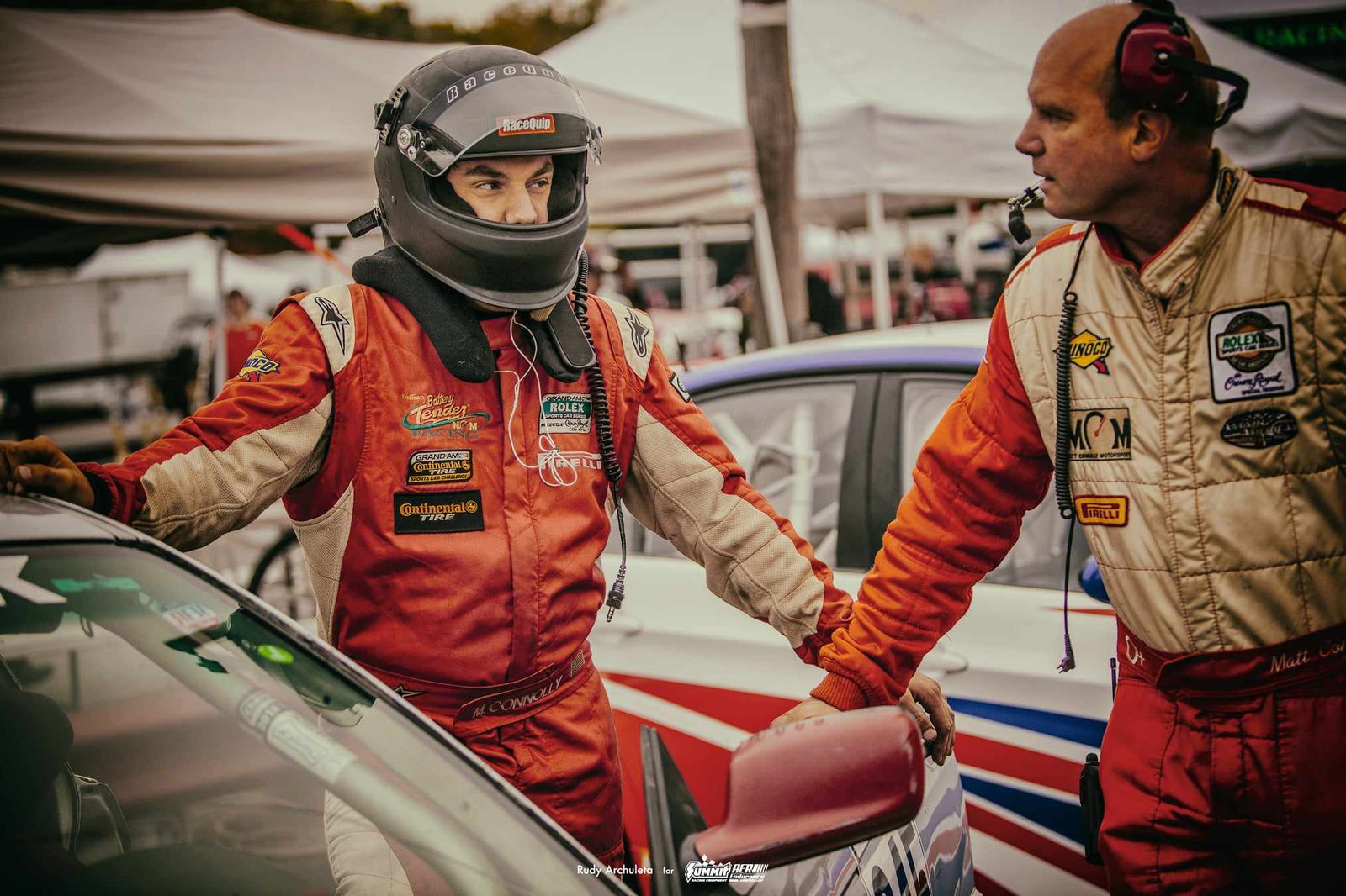 Ben and a teammate standing between BMW race cars in the paddock