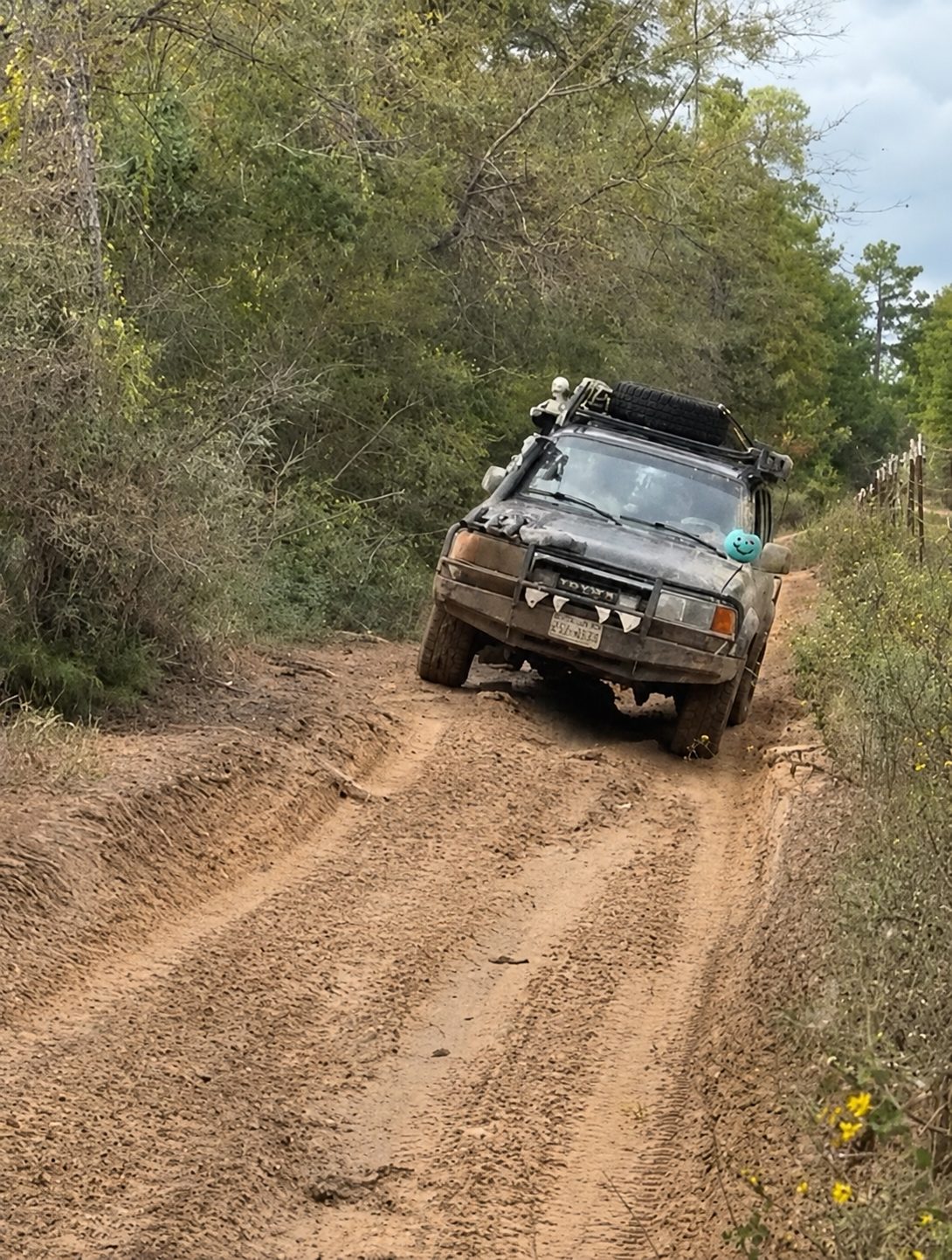 Toyota Land Cruiser driving down a dirt trail with a blue smiley ornament on the front bumper