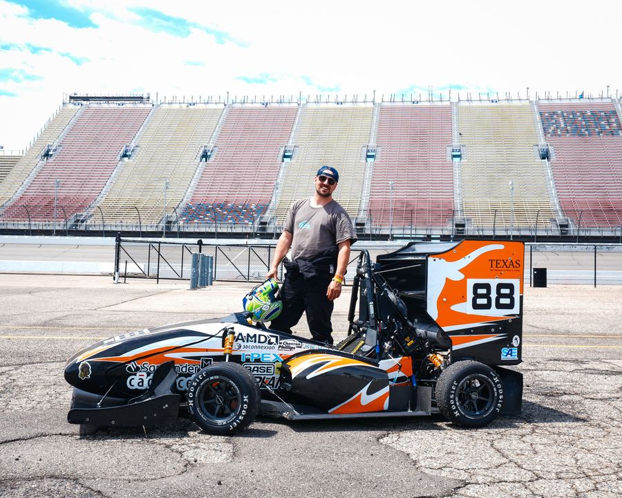 Ben standing beside the Longhorn Racing Formula SAE car in an empty grandstand