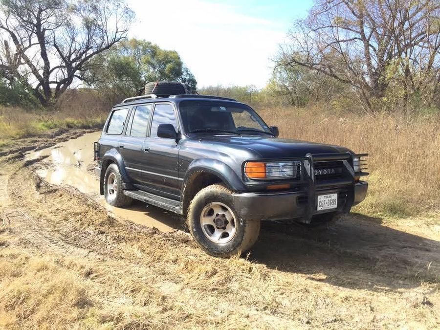 Toyota Land Cruiser parked on a rural gravel road beside a horse pasture