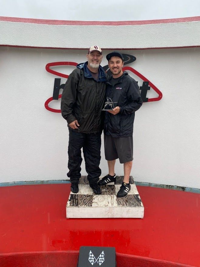Ben and a teammate on the podium holding a trophy at a race track