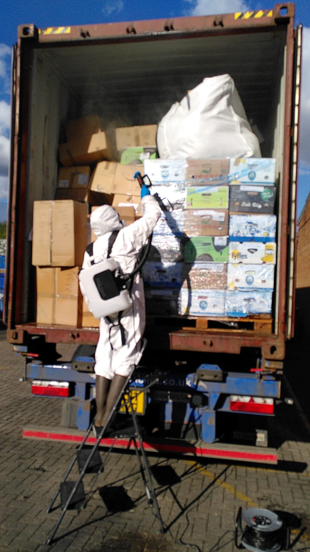 a person in PPE gear, fumigating a truck full of boxes