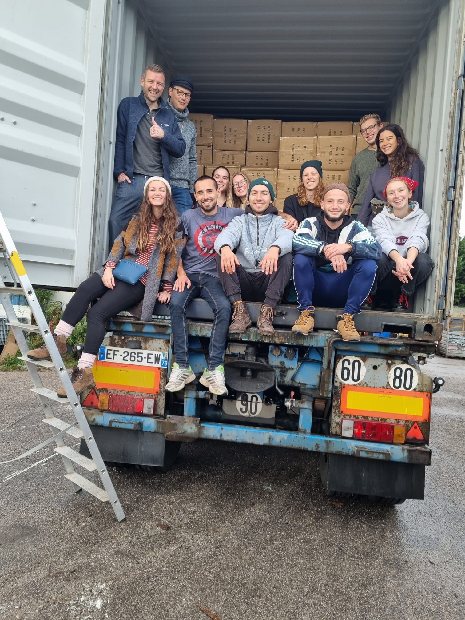 A group picture of volunteers posing inside a container full of boxes of aid donated to them