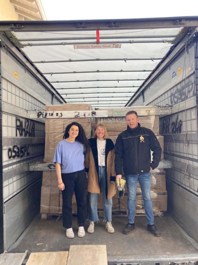 two volunteers and a truck driver posing for a photo inside a truck they have filled with boxes of donated items