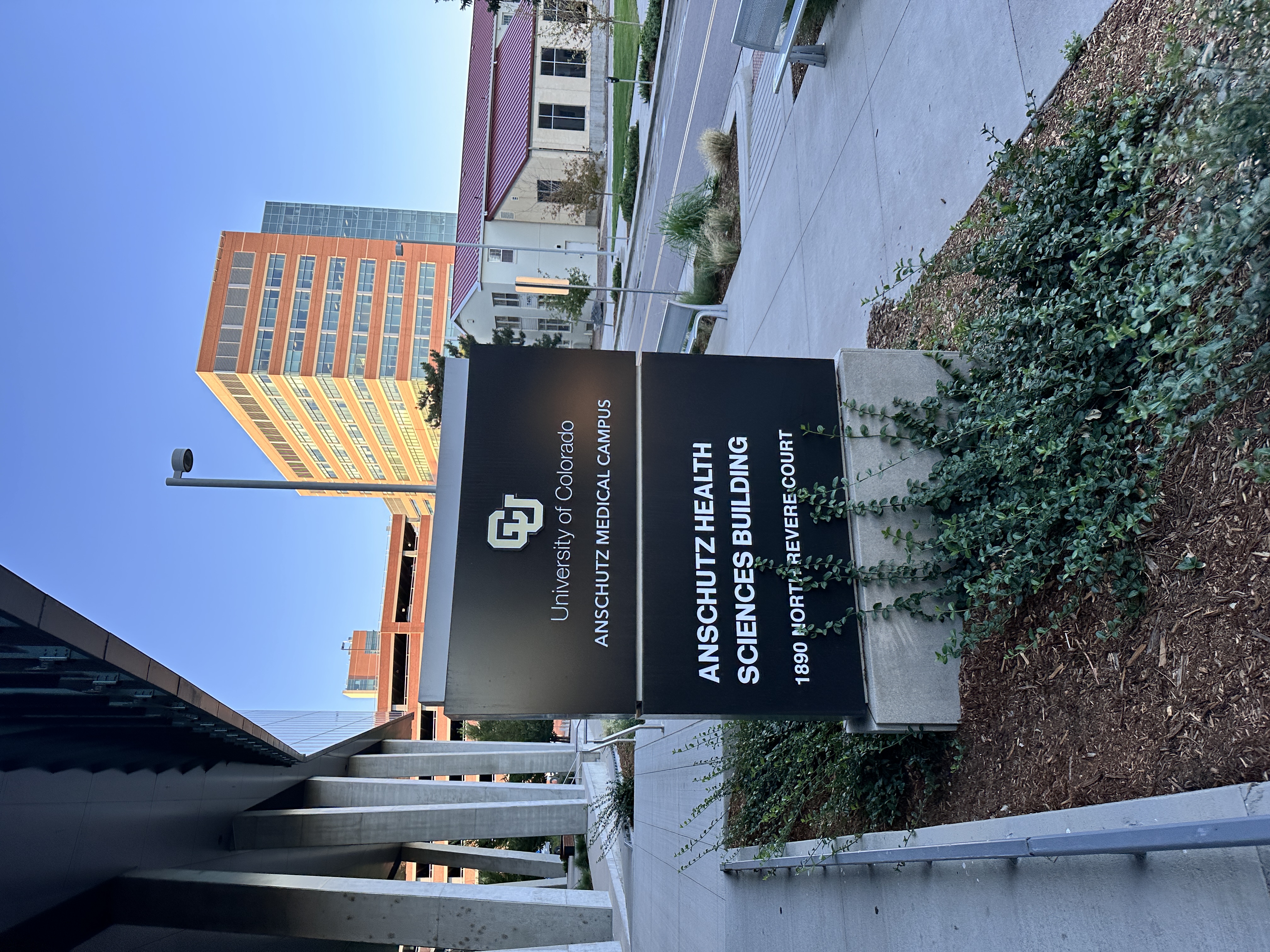 a photo of signage for the University of Colorado Anschutz Health Sciences Building outside of the building entryway with a large building int he back