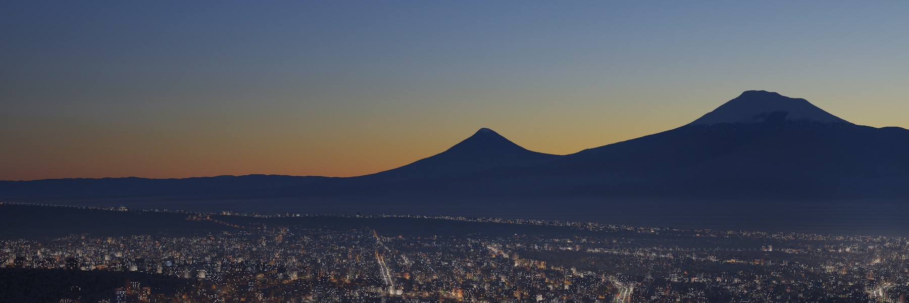 Ararat as a dark silhouette at blue hour above the street lights of Yerevan