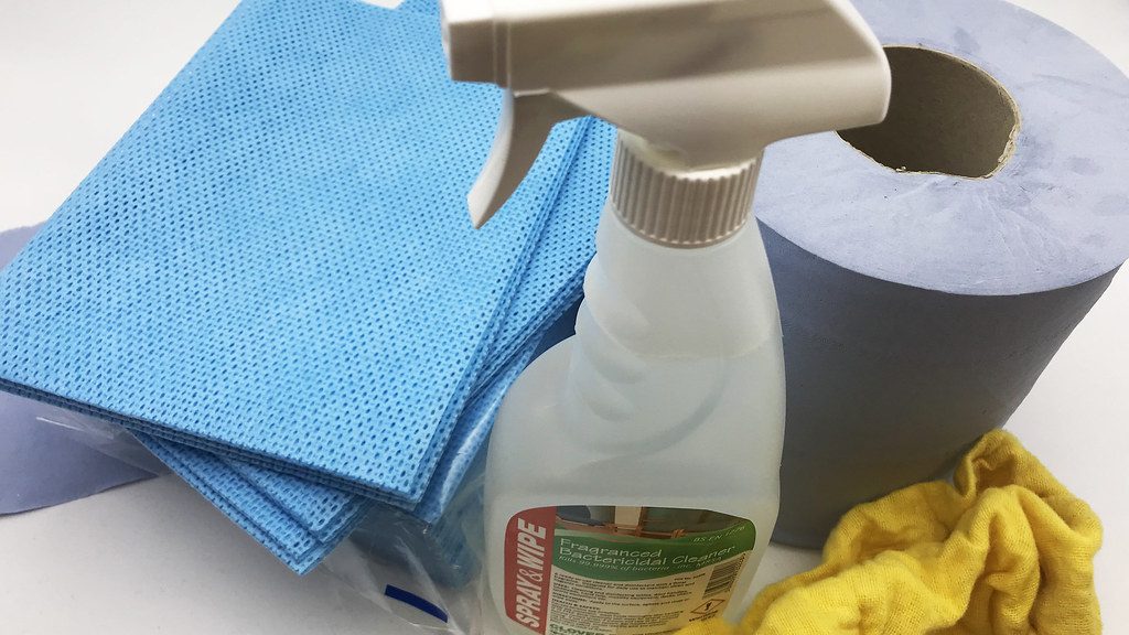 Spray bottle, blue cleaning cloths and a yellow duster on a white surface