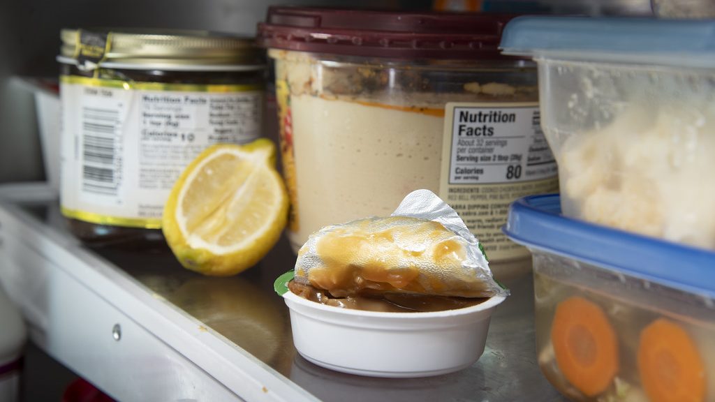Refrigerator shelf holding leftovers in sealed containers, jars and a cut lemon