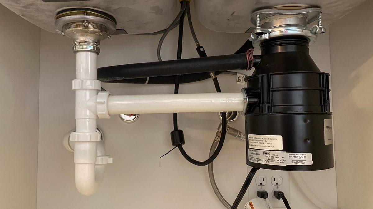 Garbage disposal unit and white drain pipes mounted under a kitchen sink