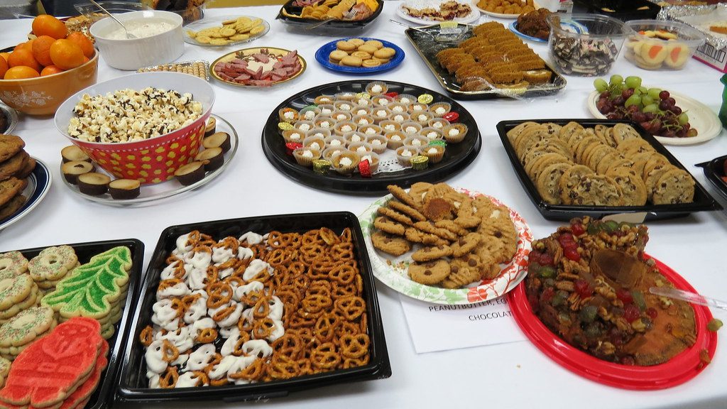 A party table crowded with platters of cookies, pretzels, sliced meats, fruit, and a bowl of dip