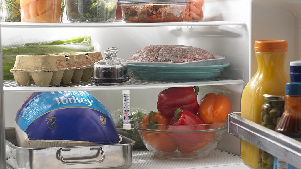 Wrapped frozen turkey in a roasting pan on the bottom shelf of an open refrigerator