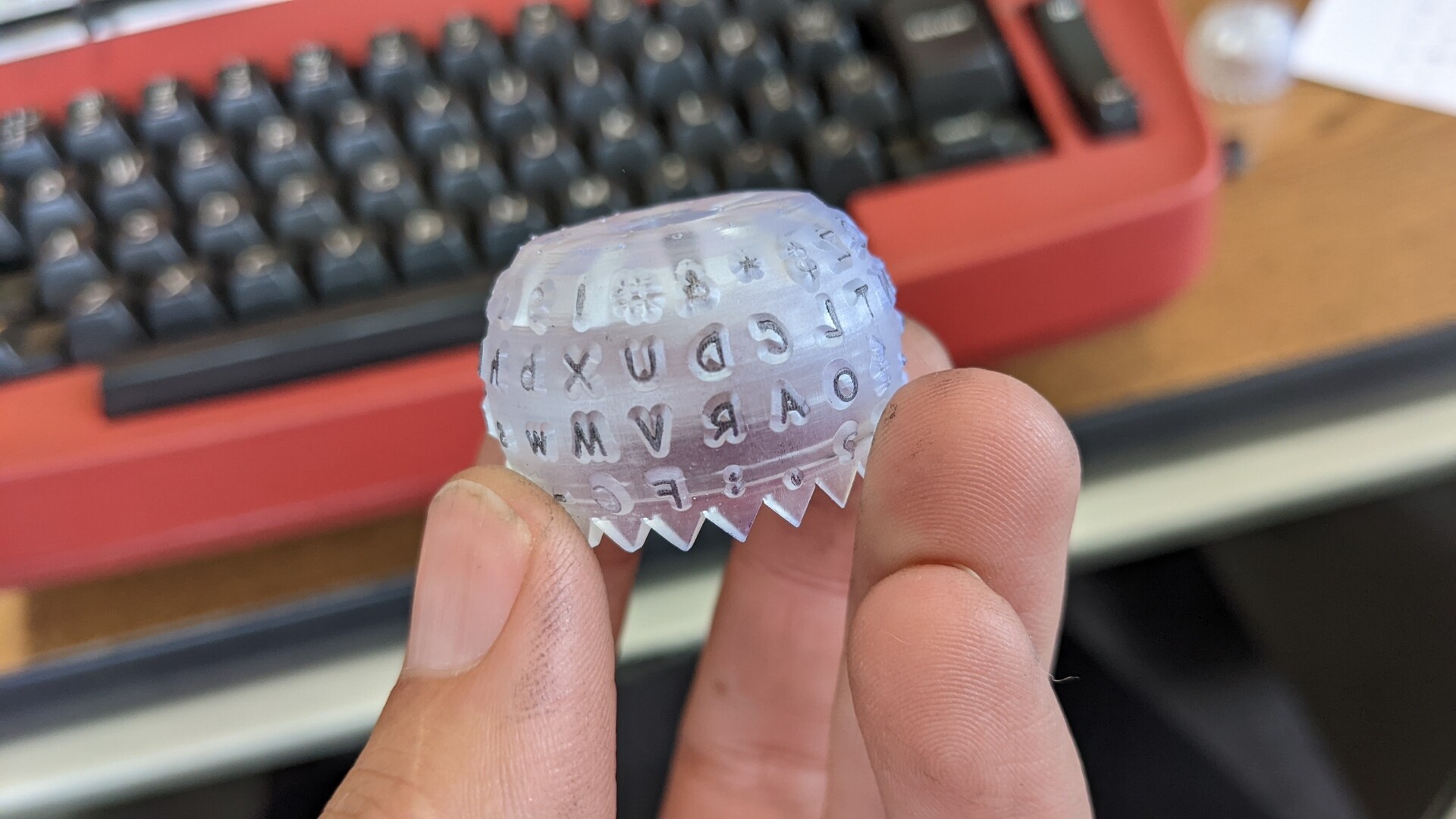 A 3D printed typeball for the IBM Selectric. The font is Comic Sans. There is ink on most of the letters.