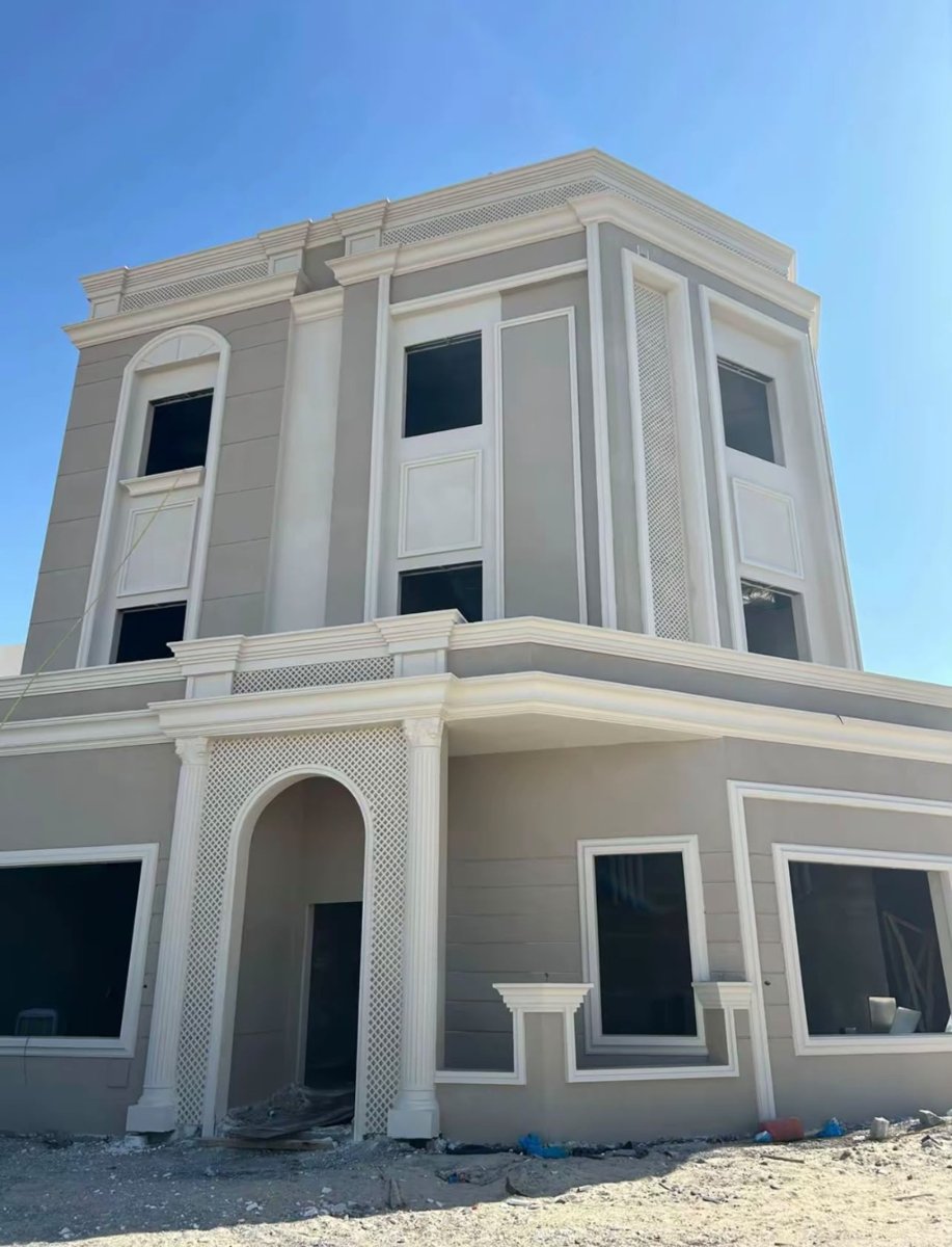 واجهة مبنى رمادية مع تفاصيل وزخارف بيضاء وفتحات نوافذ أثناء الإنشاء