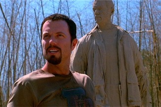 Jayne, confused, stands in front of a mud statue of himself