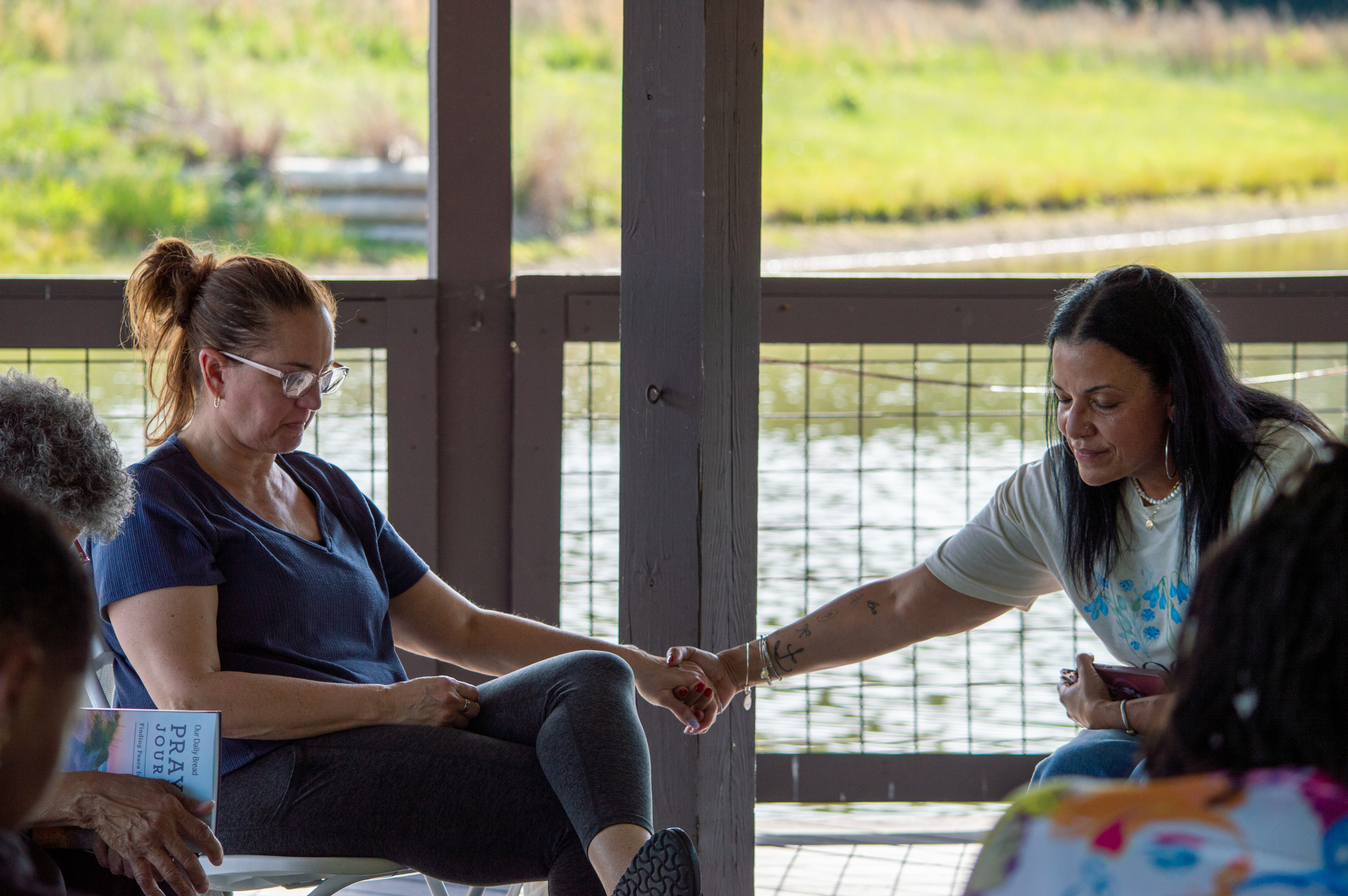 Two women holding hands in prayer beside the water