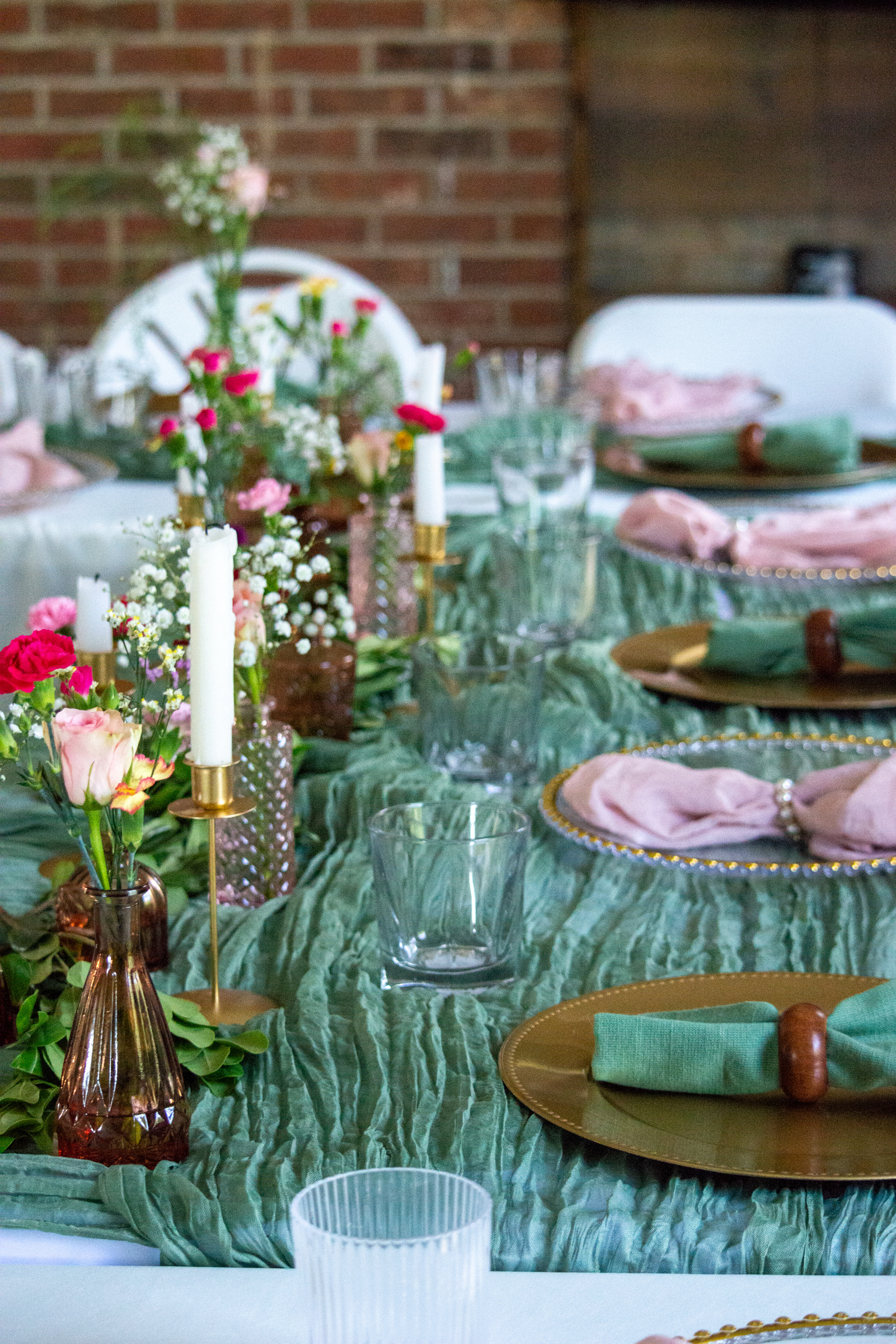 A candlelit table set with flowers, gold chargers and sage linens