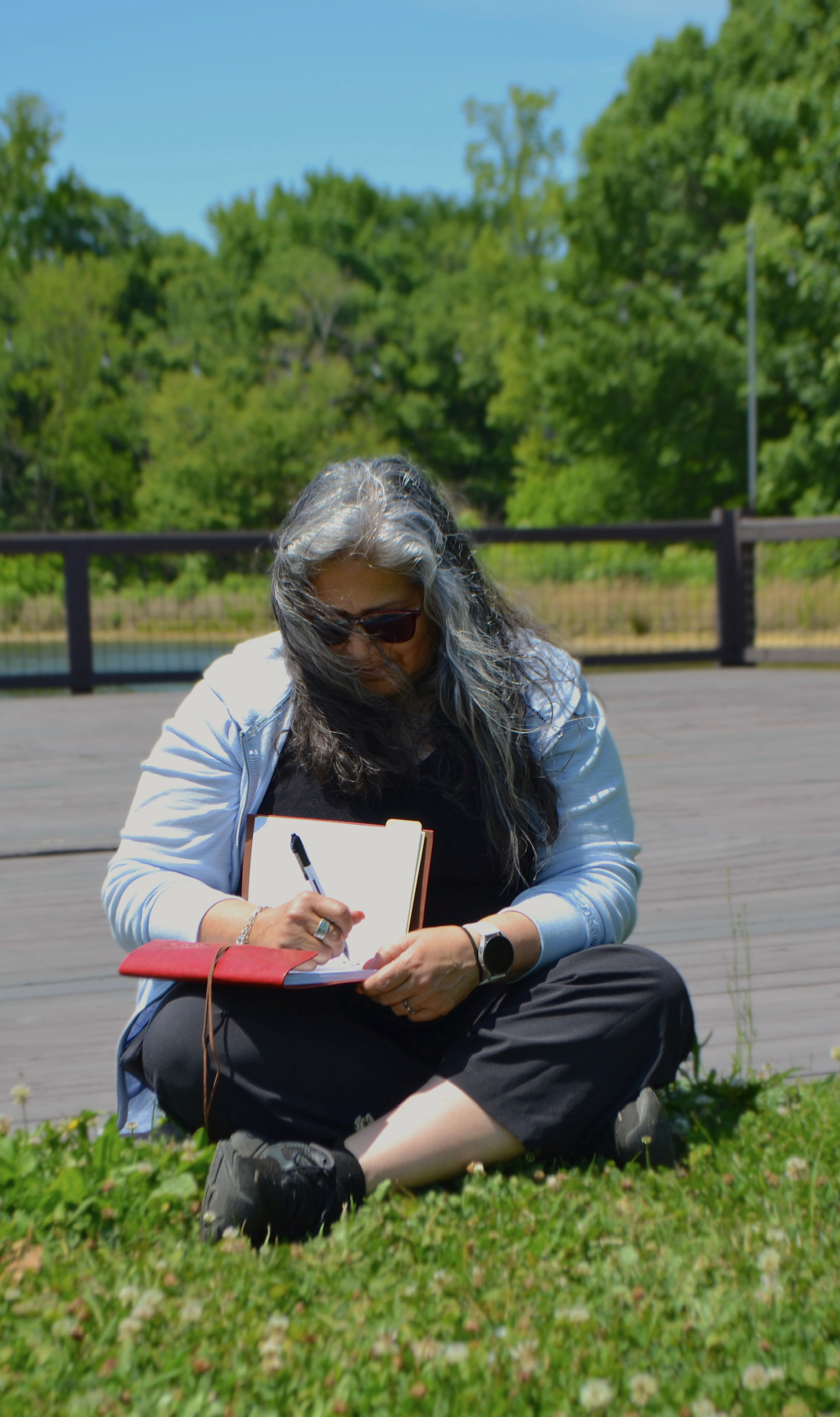 A woman journaling on the grass by the water