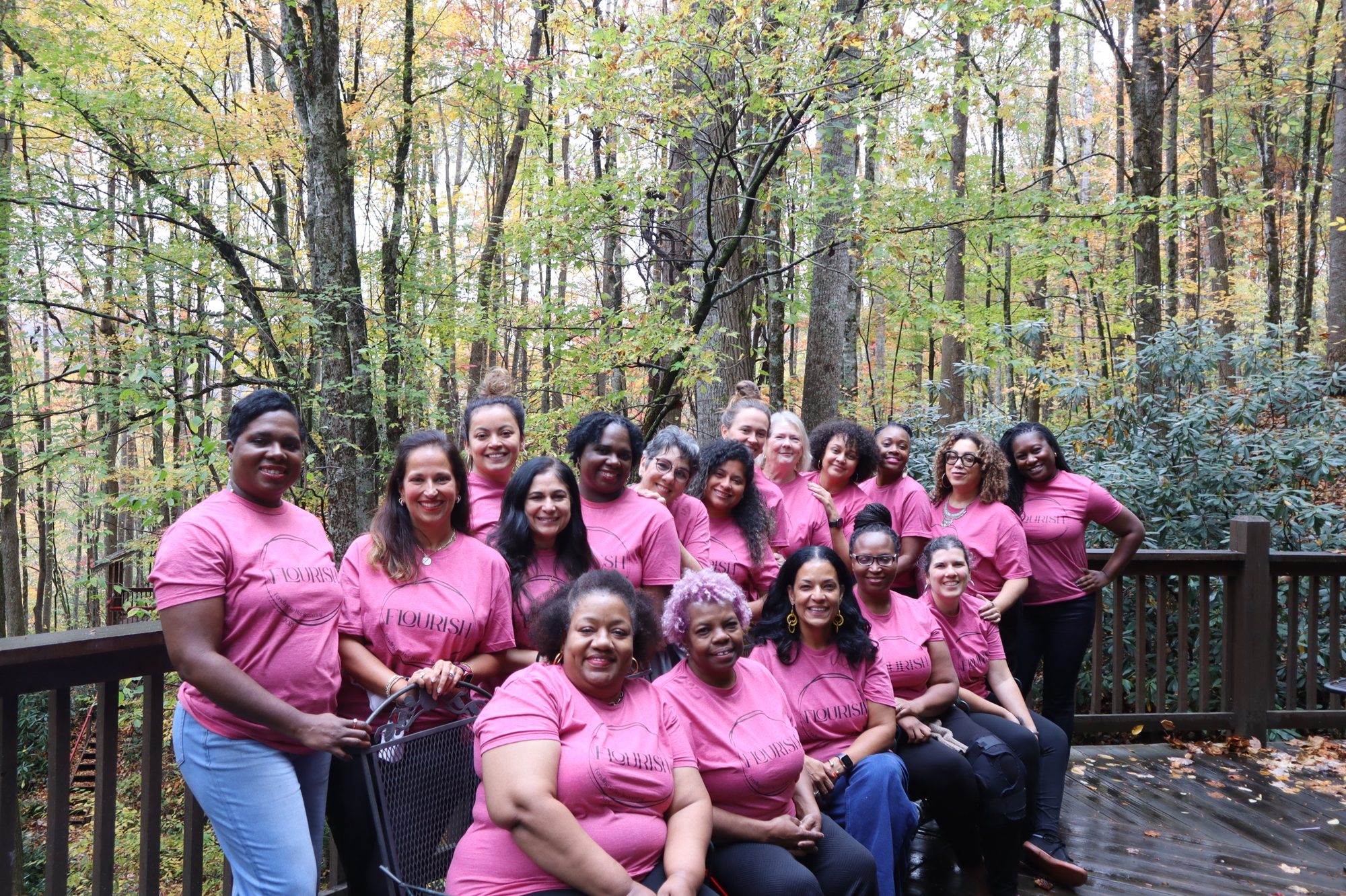 Retreat guests in pink Flourish shirts on a wooded deck in autumn