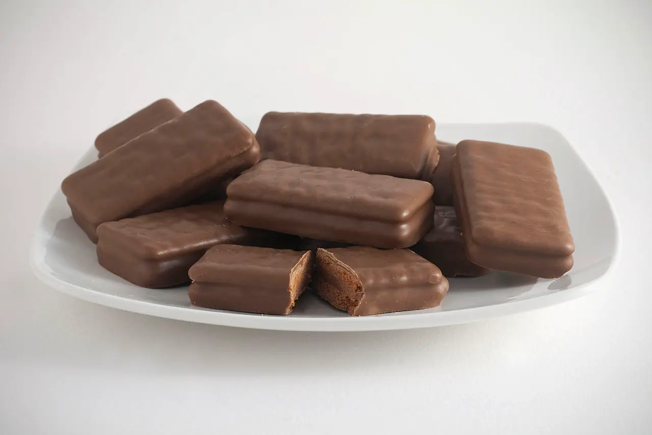 A plate of Tim Tams, with one in the centre broken open to show the biscuit and chocolate cream filling. [Photograph by Bilby](https://commons.wikimedia.org/wiki/File:Tim_Tams.jpg). Licensed under the [Creative Commons Attribution-Share Alike 3.0][creativecommons] license.