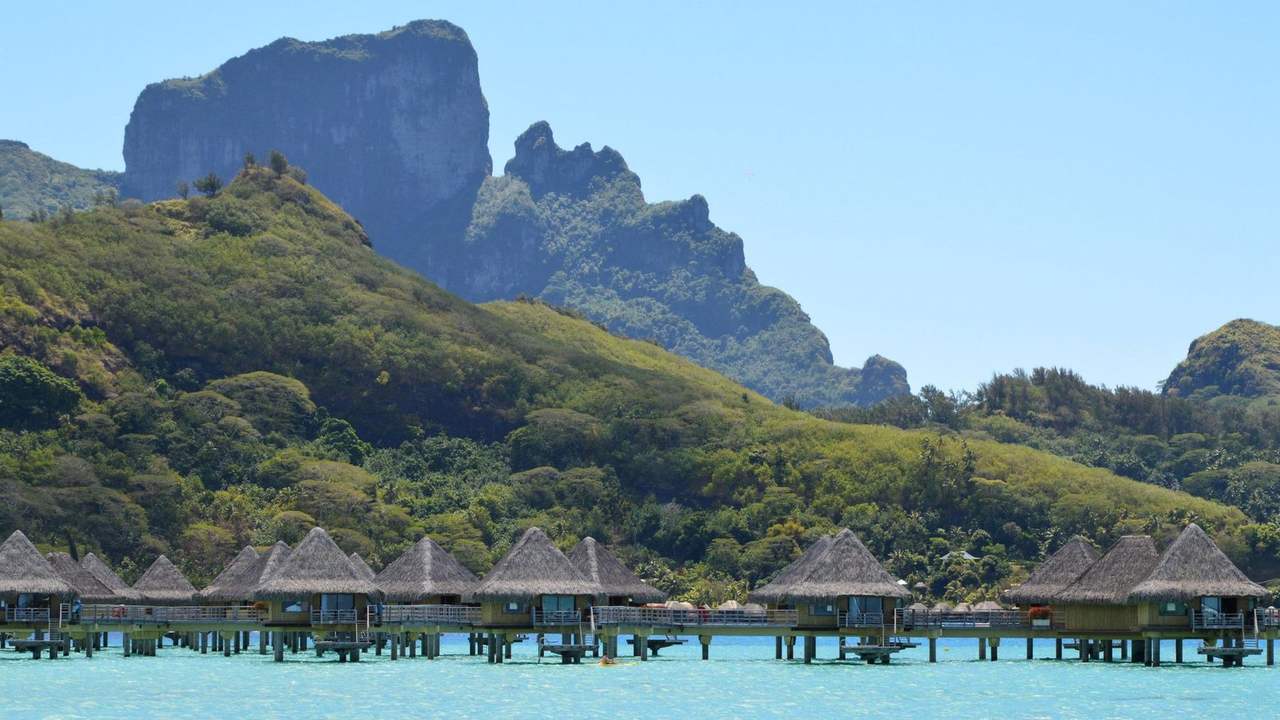 Overwater bungalows and Mount Otemanu, Bora Bora lagoon, day, clear blue sky