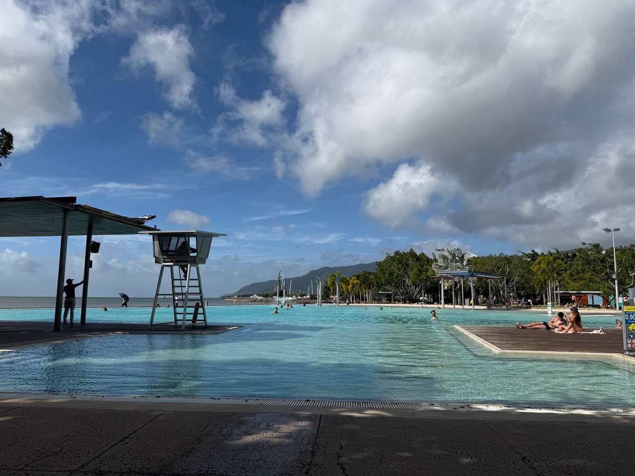 Cairns Esplanade Lagoon with woven fish sculptures and mountains, day, blue sky