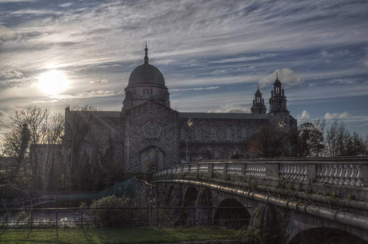 Galway Cathedral dome across Salmon Weir Bridge, day, pale blue sky with clouds