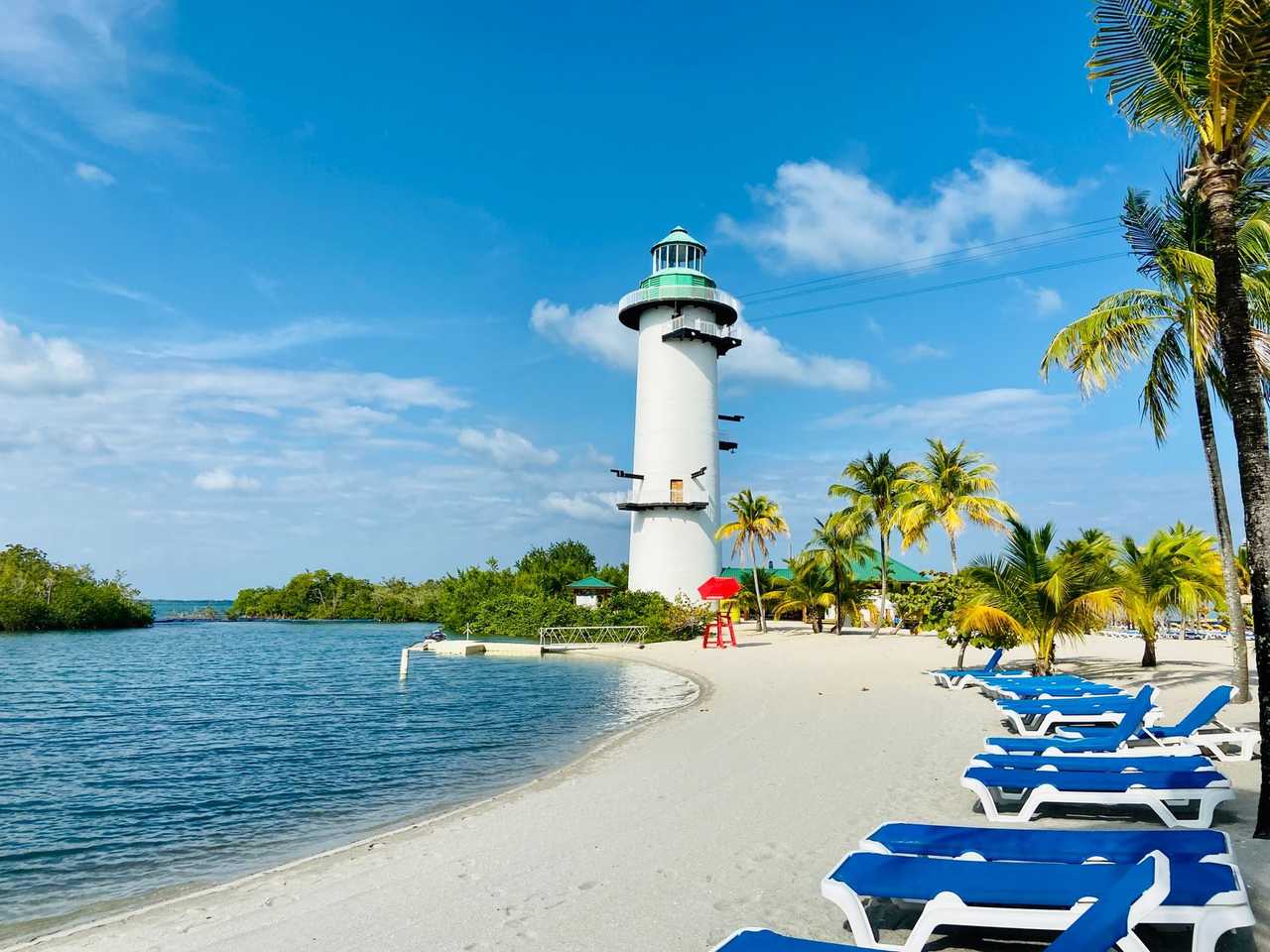 Harvest Caye identifiable white lighthouse with zipline platforms and palm beach, day, blue sky