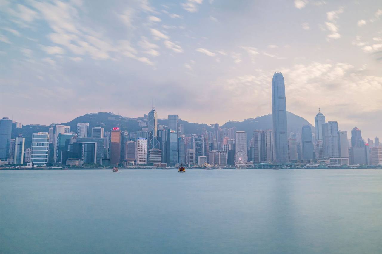 Hong Kong Island skyline across Victoria Harbour (IFC, Bank of China), day, pale blue sky