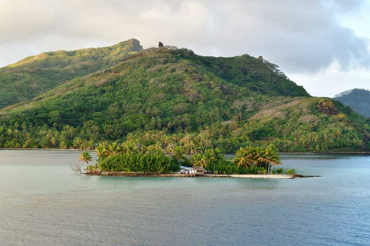 Huahine motu and volcanic ridge across lagoon, day, pale blue sky