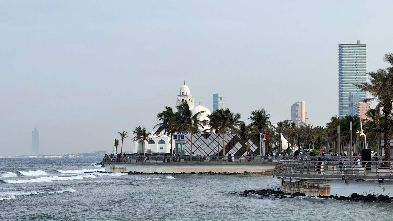 Jeddah Corniche waterfront with Al-Rahma Mosque domes/minaret and palm trees, day, pale blue sky