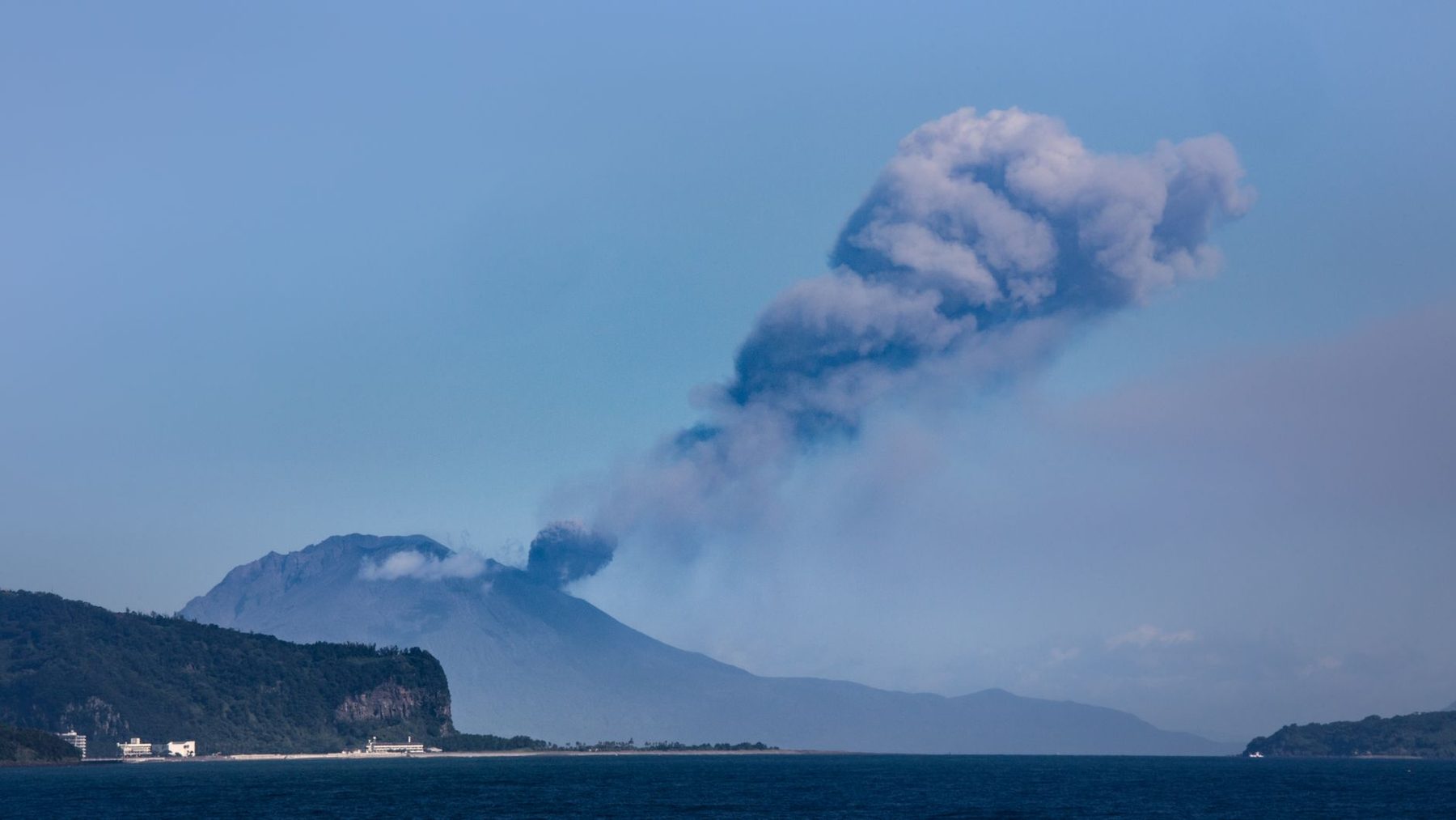 Sakurajima erupting across Kagoshima Bay, day, clear blue sky