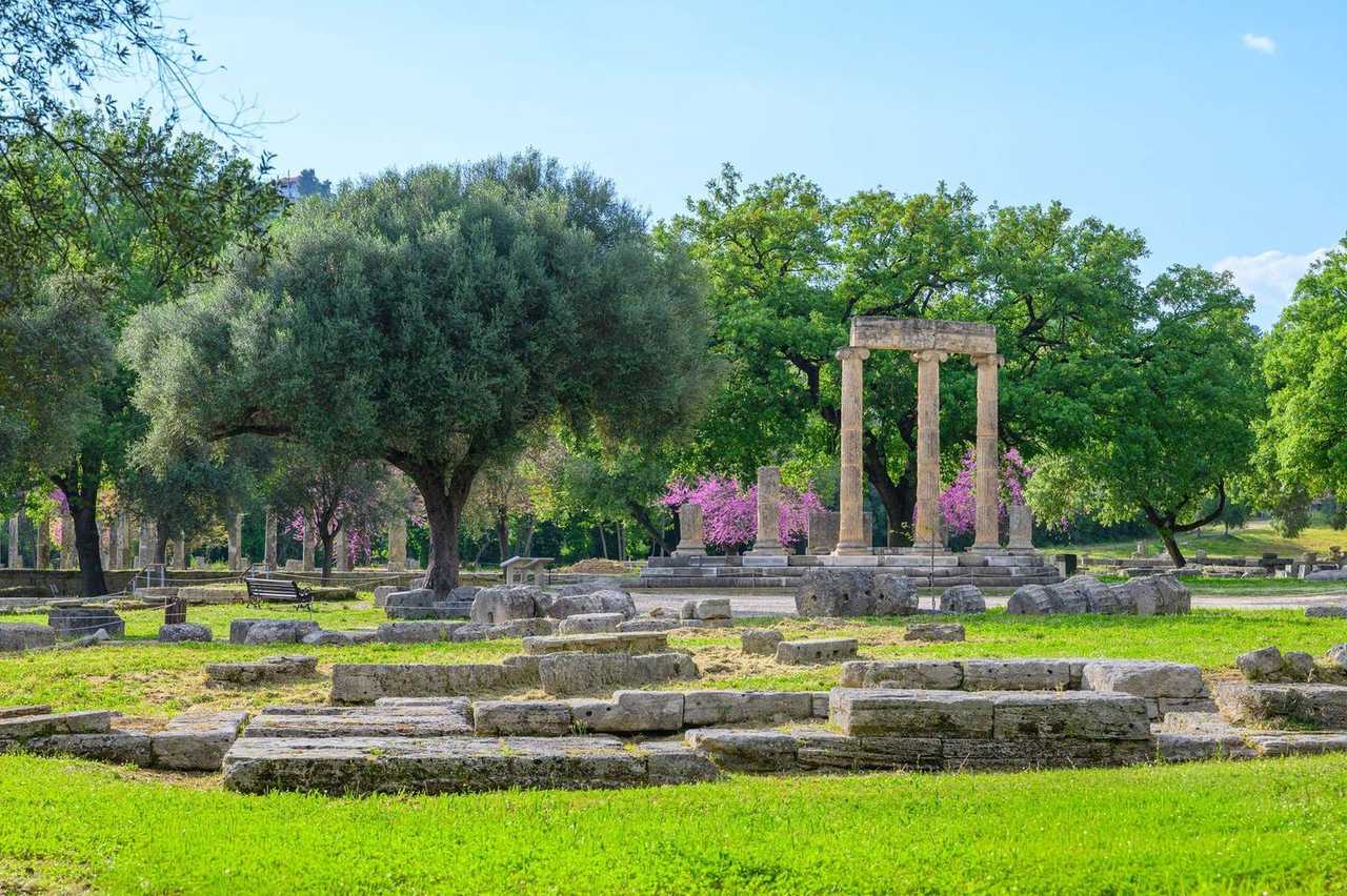 Ancient Olympia columns among trees, day, blue sky