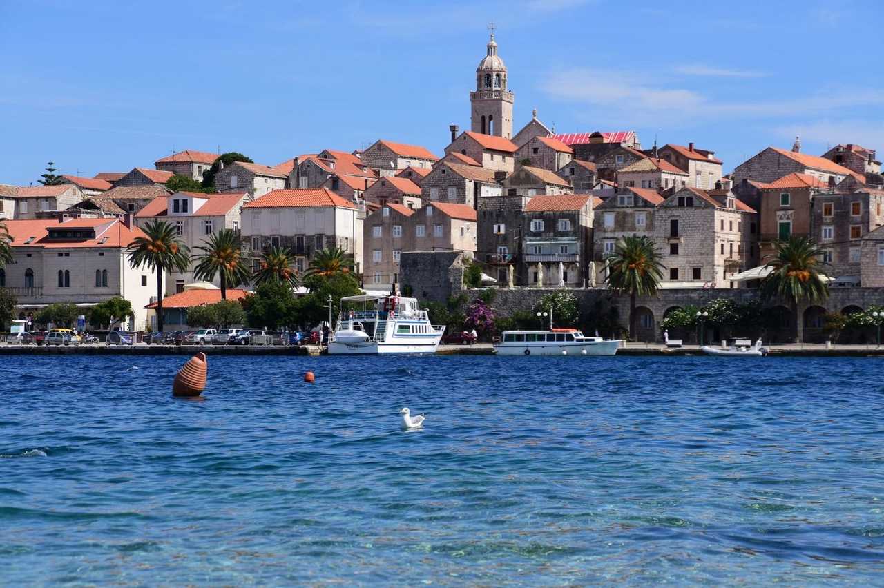 Korčula old town stone buildings and church tower from the water, day, solid blue sky