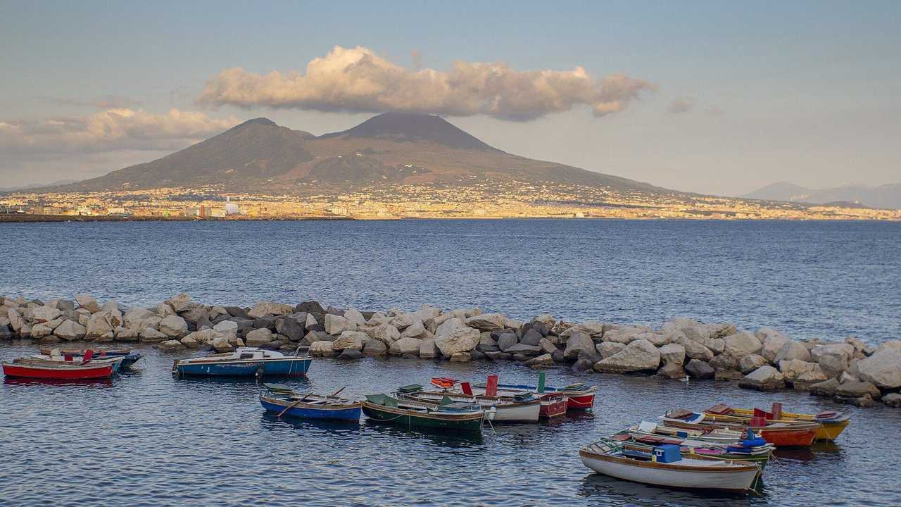Naples + Vesuvius from the lungomare / small-boat harbour, day, pale blue sky