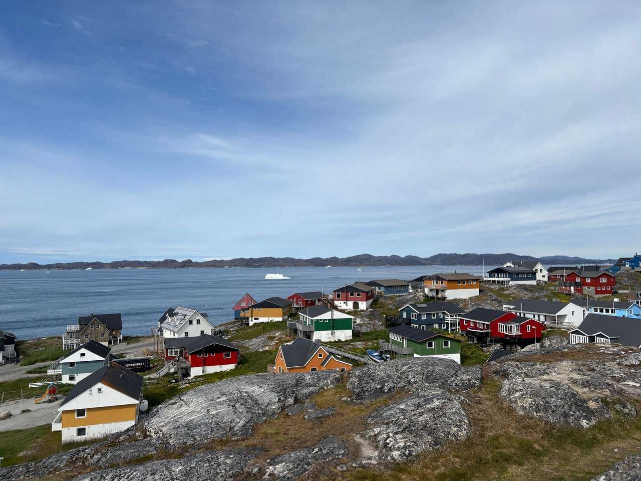 Nuuk colourful wooden houses on rocky coast overlooking fjord ice, day, pale blue sky