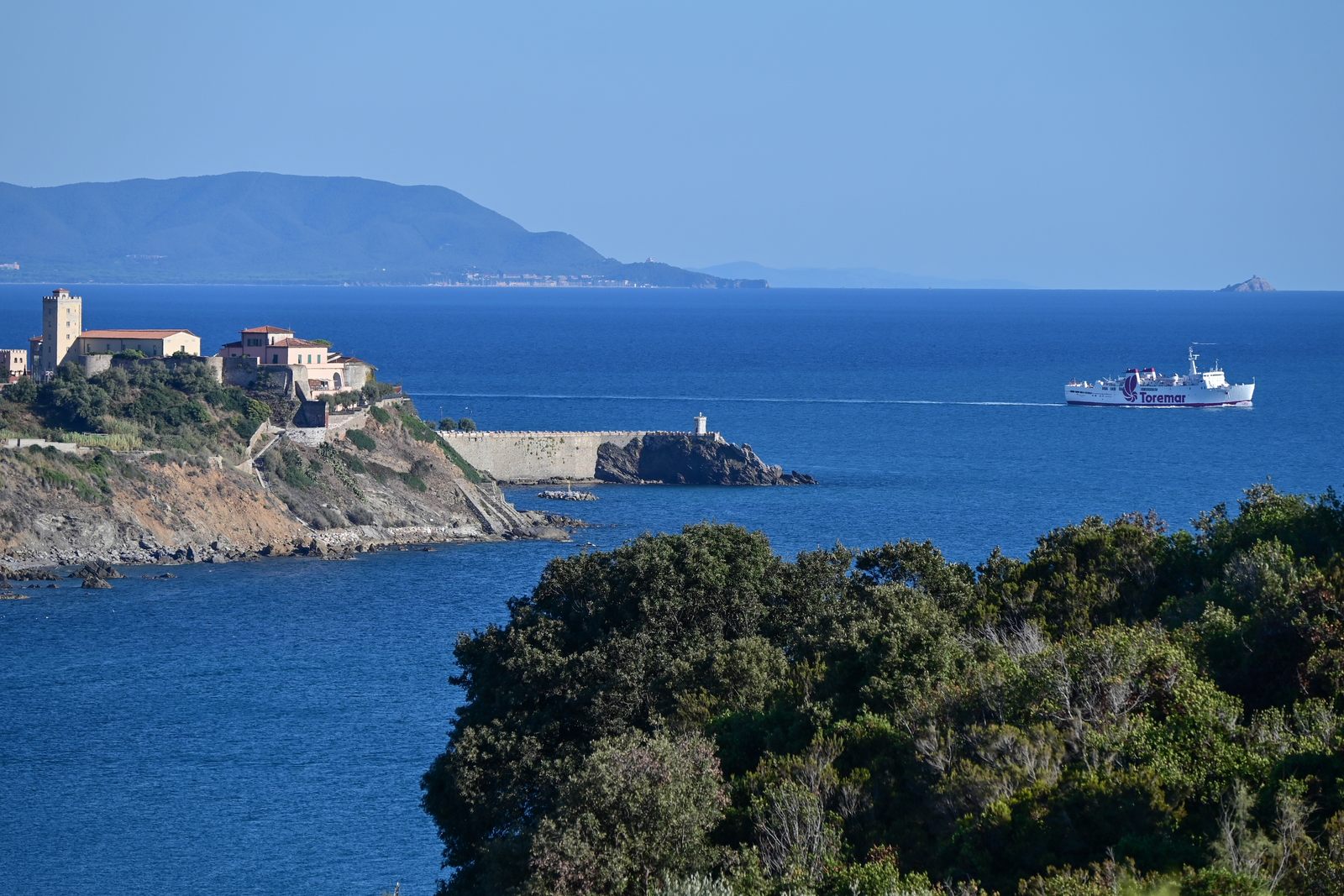 Piombino coastal townscape with terracotta roofs and Torrione-style tower from the water, day, clear blue sky