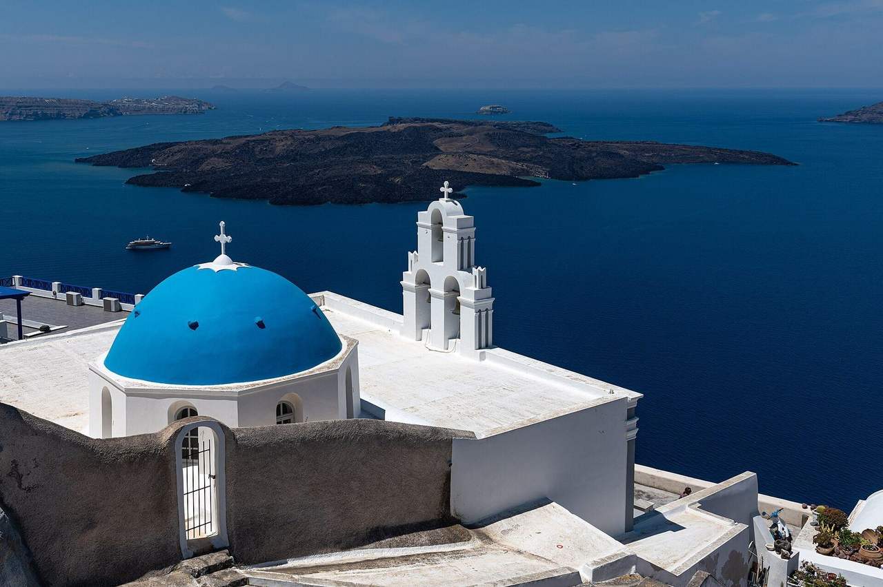 Blue-domed church overlooking the Santorini caldera, day, clear pale blue sky