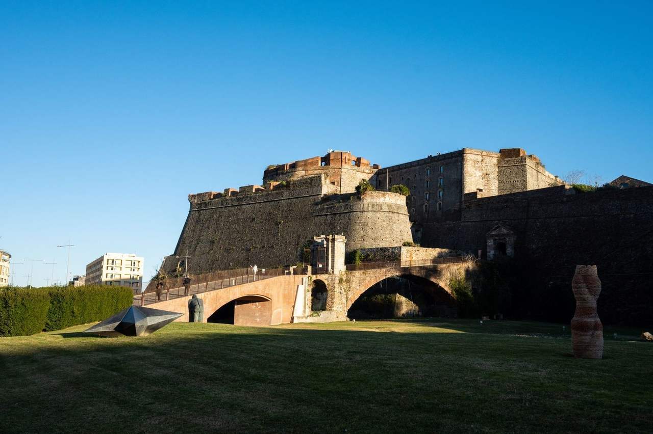 Priamar Fortress stone walls and bridge over lawn sculptures, Savona, day, solid blue sky